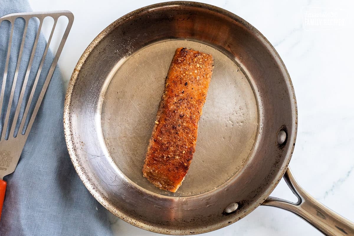 Skillet with grilled pecan Salmon piece and spatula on the side.