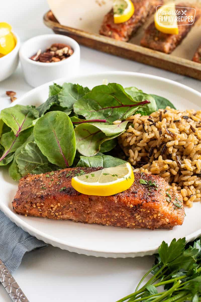 Pecan salmon garnished with a lemon slice on a plate with rice and salad.