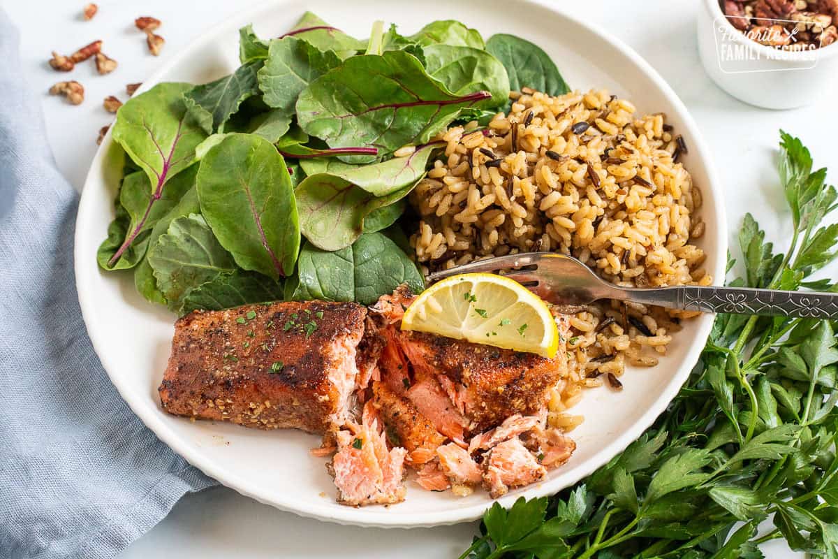 Pecan salmon garnished with a lemon slice on a plate with rice and salad.