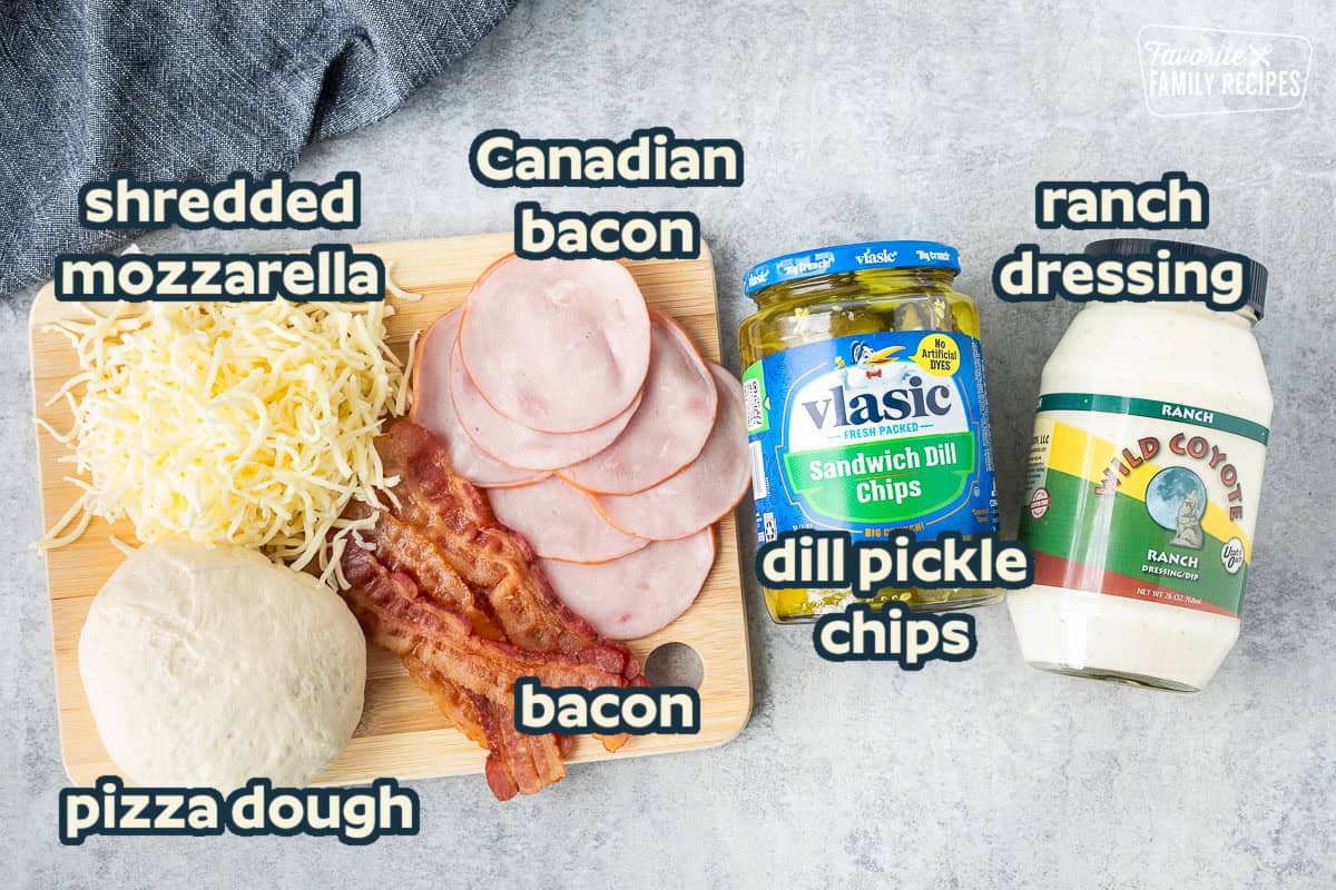 Ingredients to make Pickle Pizza including pizza dough, mozzarella cheese, bacon, Canadian bacon, pickles and ranch dressing.
