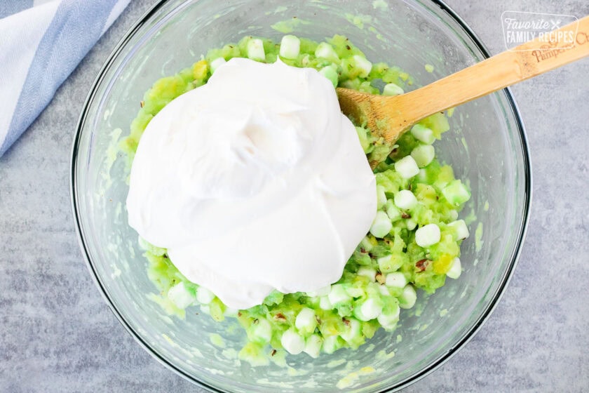 Adding cool whip to bowl of pistachio salad mixture.