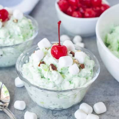 Small serving bowls of pistachio salad topped with marshmallows, chopped pecans and maraschino cherries.