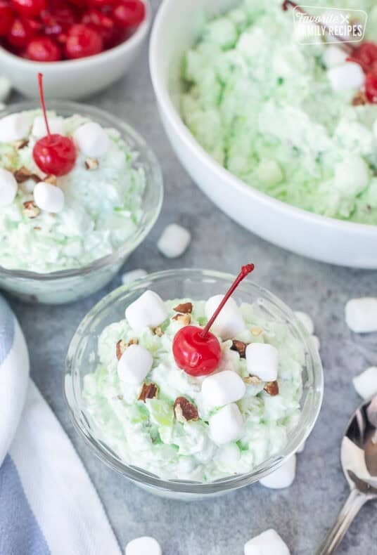 Small serving bowls of pistachio salad topped with marshmallows, chopped pecans and maraschino cherries.