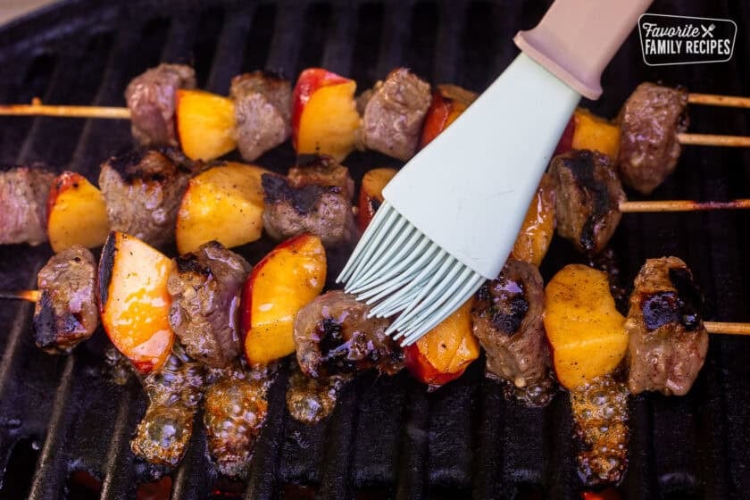 Basting pork and nectarine kabobs with honey on the barbecue.