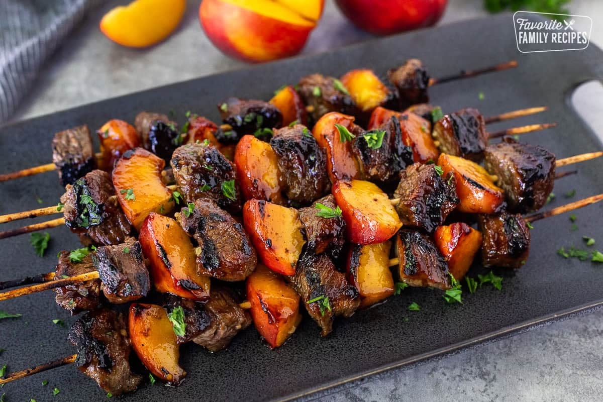 Grilled pork and nectarine kabobs on a platter and garnished with parsley.