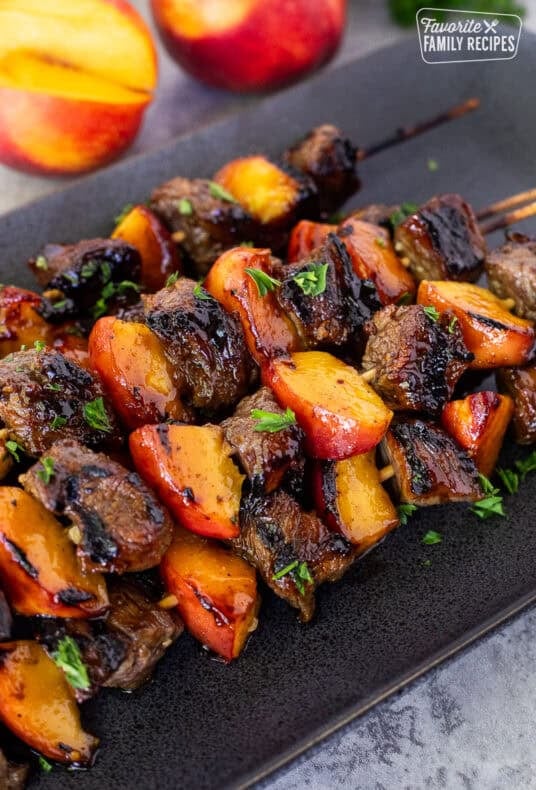 Grilled pork and nectarine kabobs on a platter and garnished with parsley.