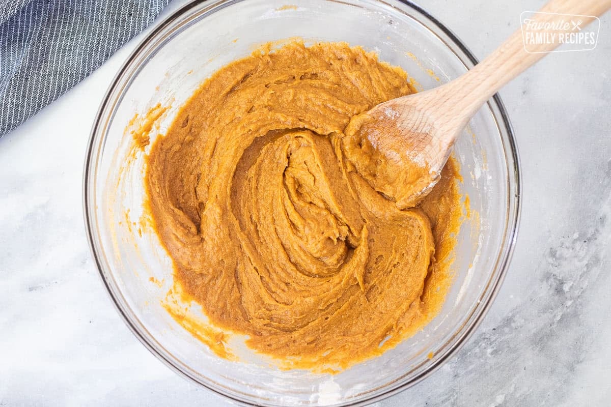 Glass mixing bowl with pumpkin chocolate chip muffin batter and a wooden spoon.