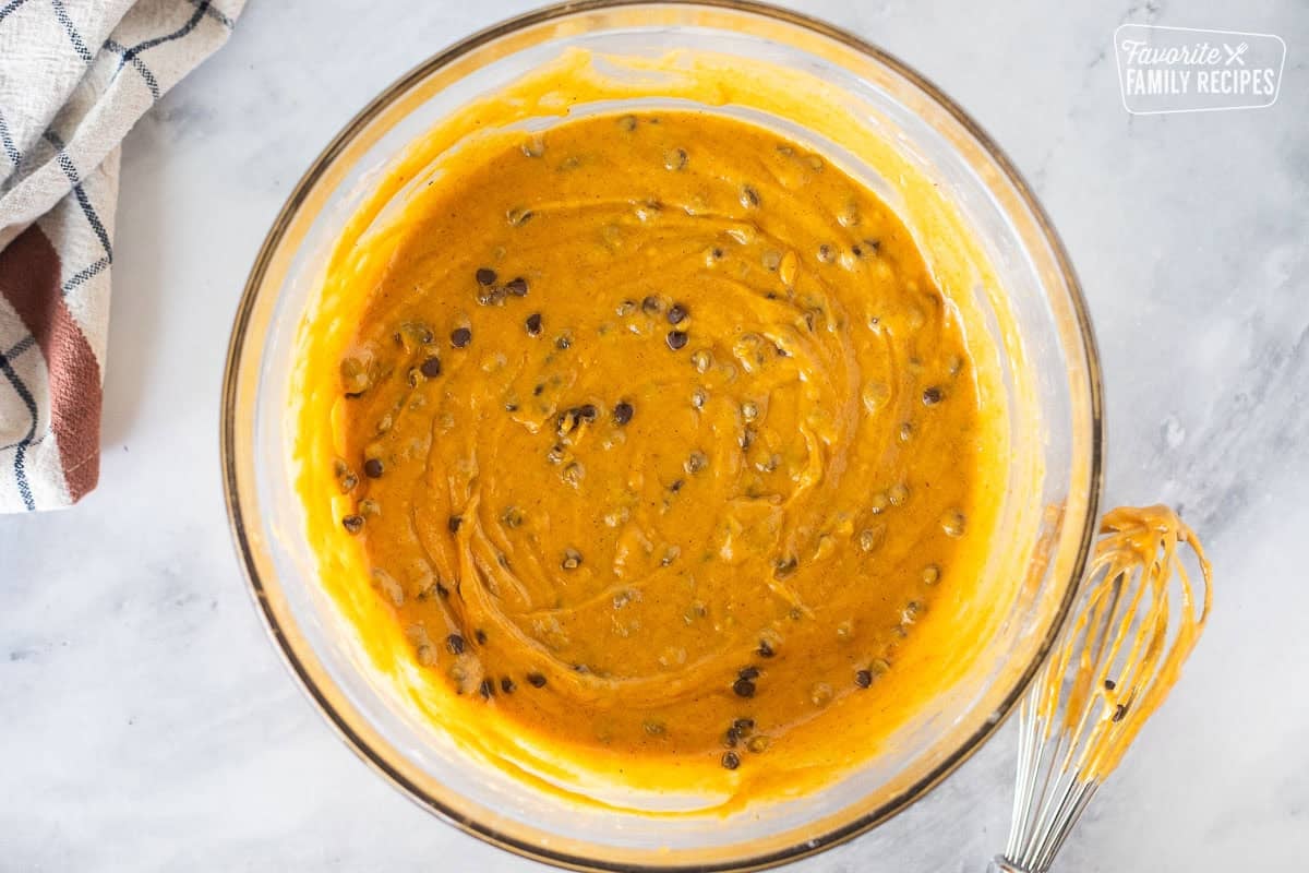 Glass mixing bowl with pumpkin coffee cake batter and mini chocolate chips. Whisk on the side.