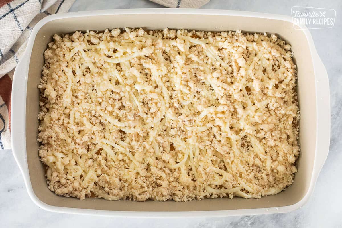 Baking dish with crumb topping on top of pumpkin coffee cake batter with cream cheese swirl.