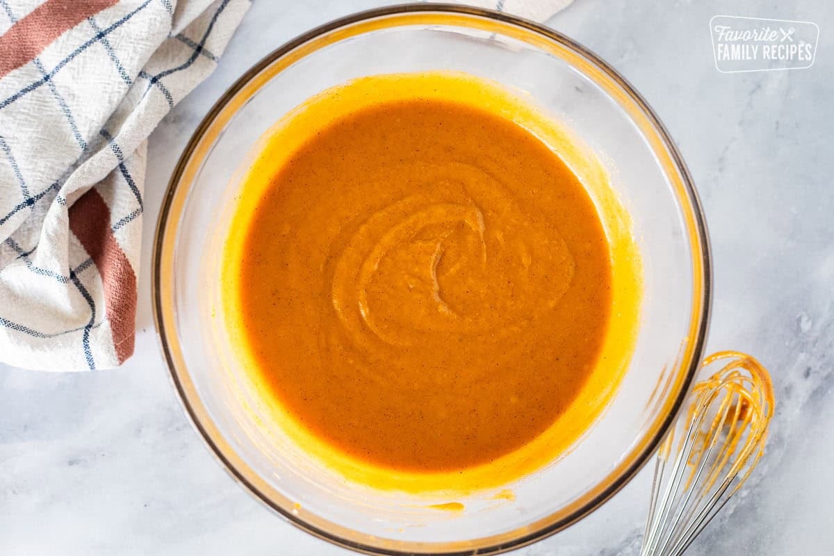 Glass mixing bowl with pumpkin mixed with sugar, oil and spice. Whisk on the side.