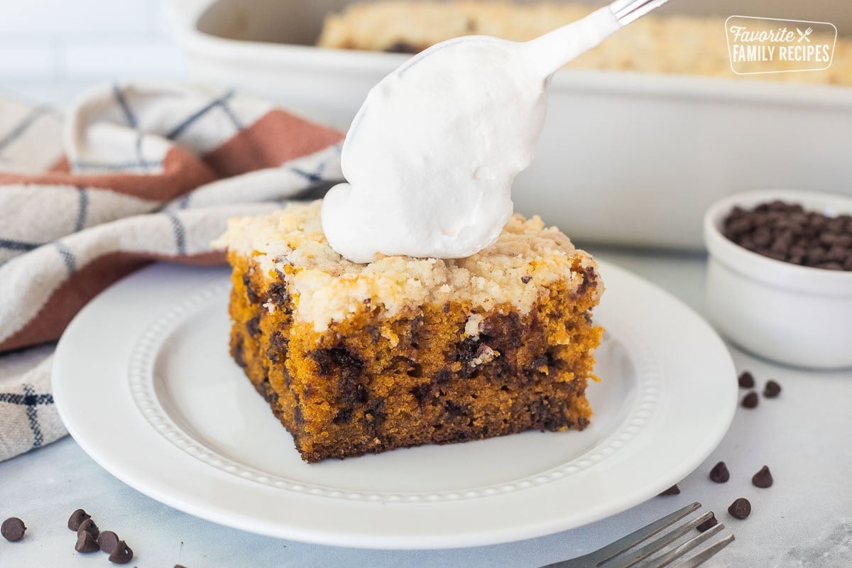 Placing all of dollop of whipped topping on a slice of pumpkin coffee cake on a plate.