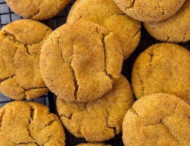 Baked pumpkin snickerdoodle cookies stacked together on a cooling rack.