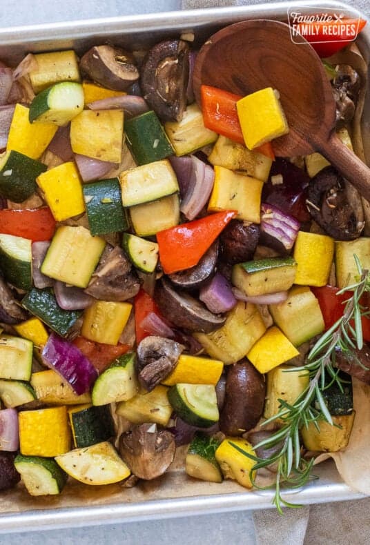 Sheet pan of roasted vegetable vegetables with a wooden spoon.