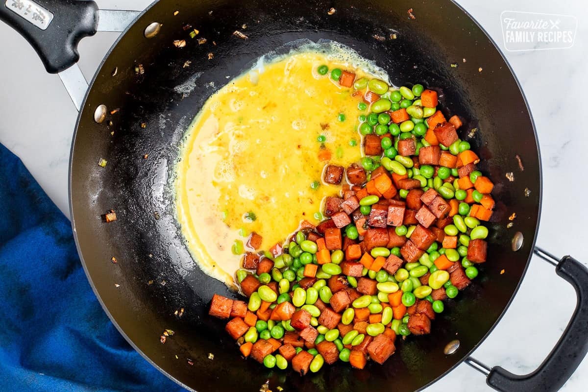 Wok with cooked vegetables, spam and whisked cracked eggs.