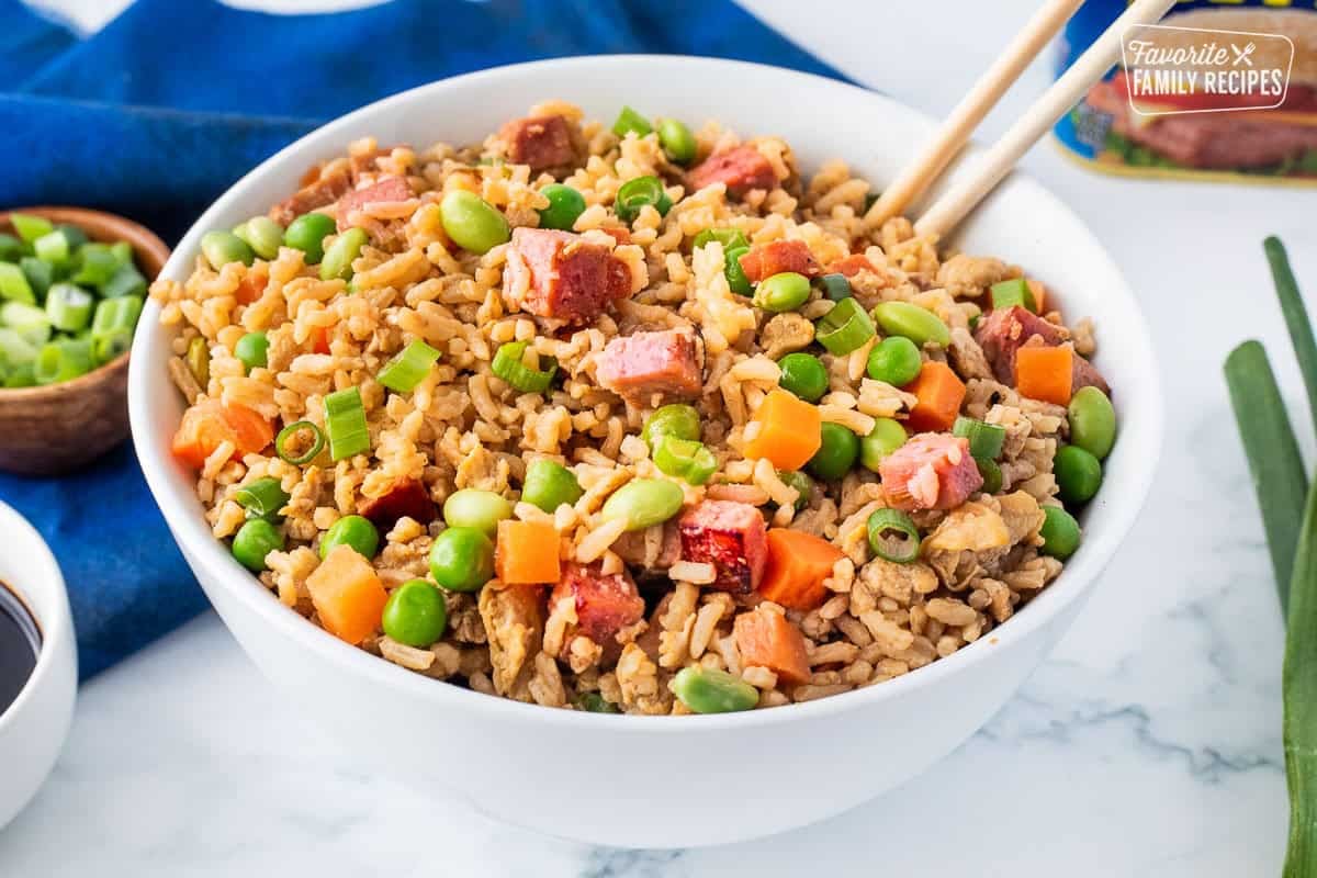 Bowl of spam fried rice and chop sticks with spam, carrots, peas, green onions, soy beans and scrambled eggs.