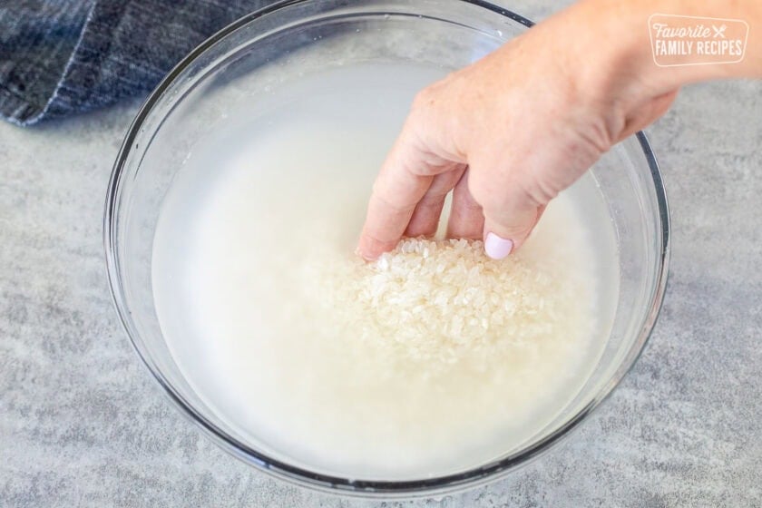 Mixing sushi rice and water by hand in a glass bowl.