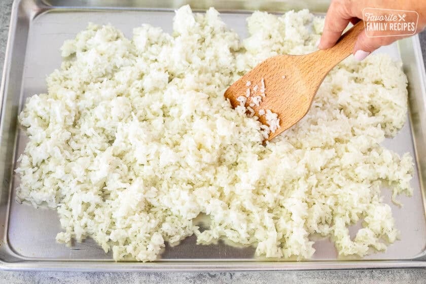 Sheet pan with spread out sushi rice and a wooden spatula.
