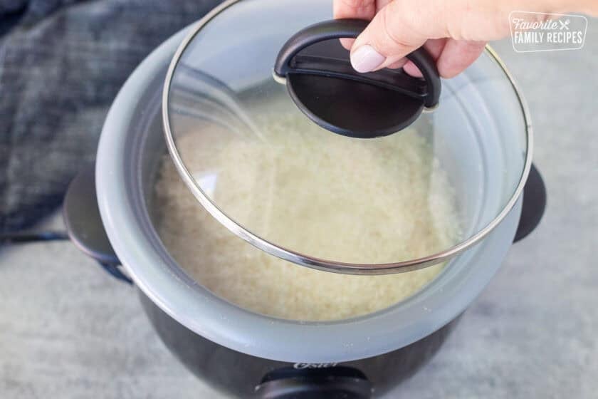 Putting the lid on a rice cooker with sushi rice and water inside.
