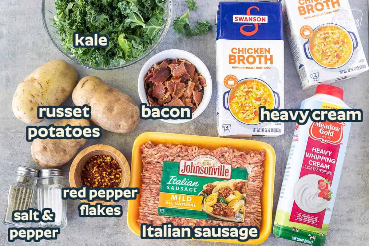 Ingredients to make Zuppa Toscana including Italian sausage, chicken broth, heavy whipping cream, bacon, potatoes, kale, red pepper flakes, salt and pepper.