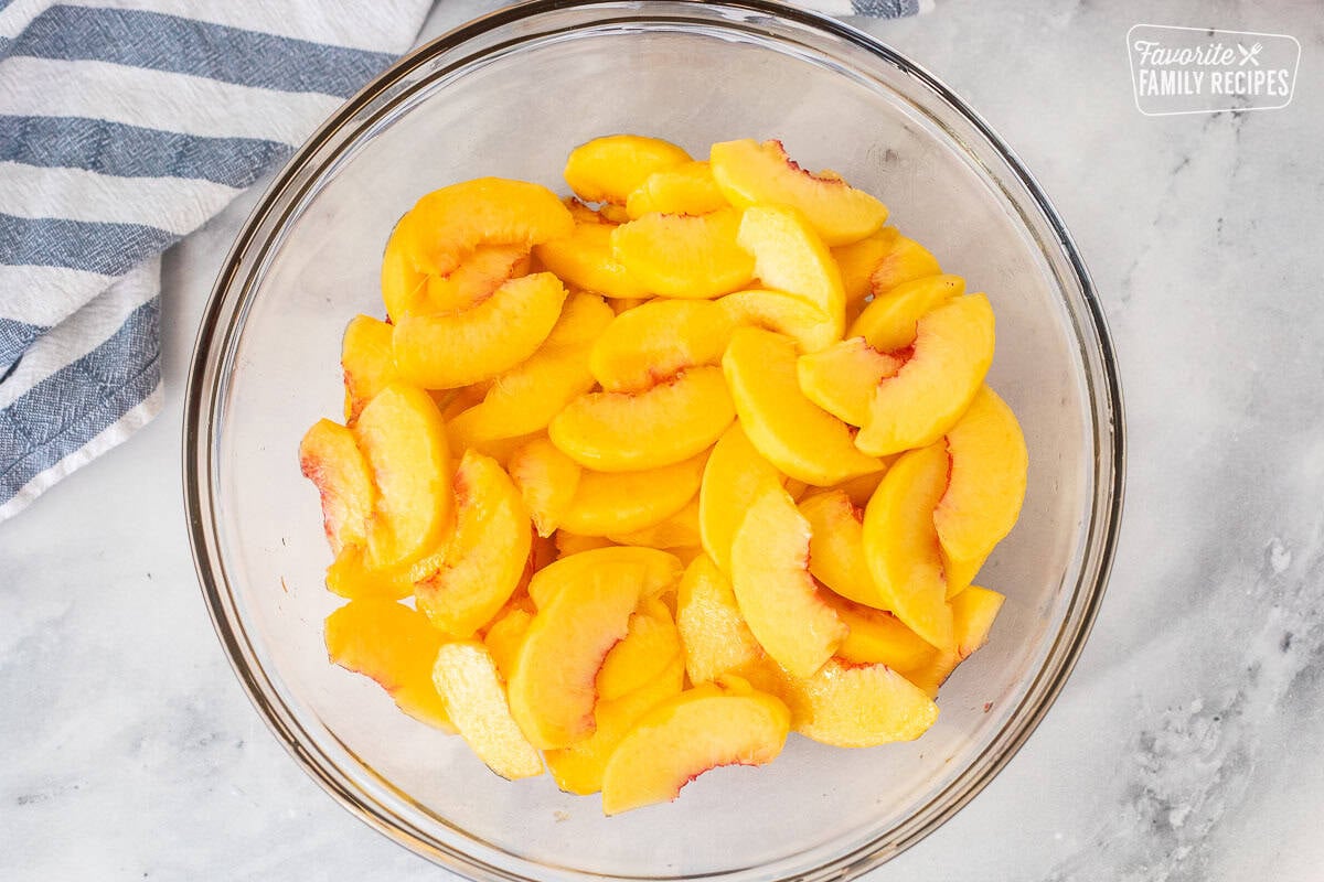 Glass bowl with peeled and sliced peaches.