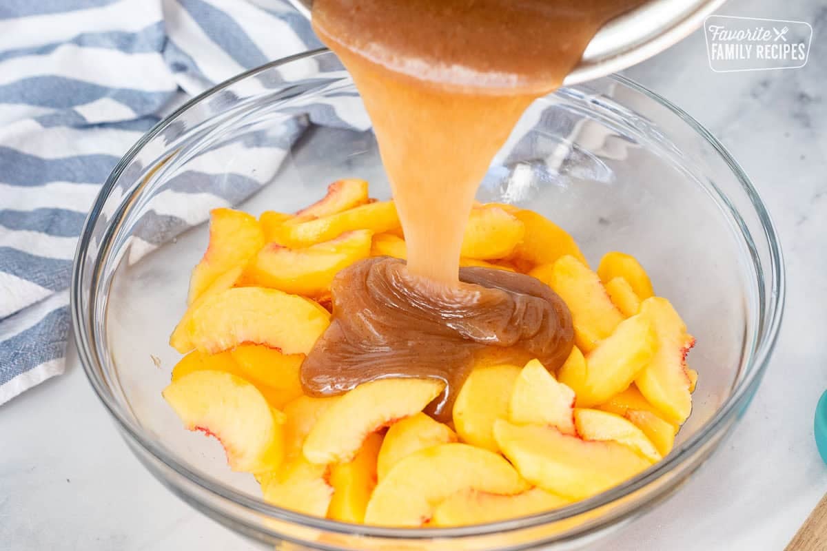 Pouring hot cinnamon glaze onto bowl of fresh peaches.