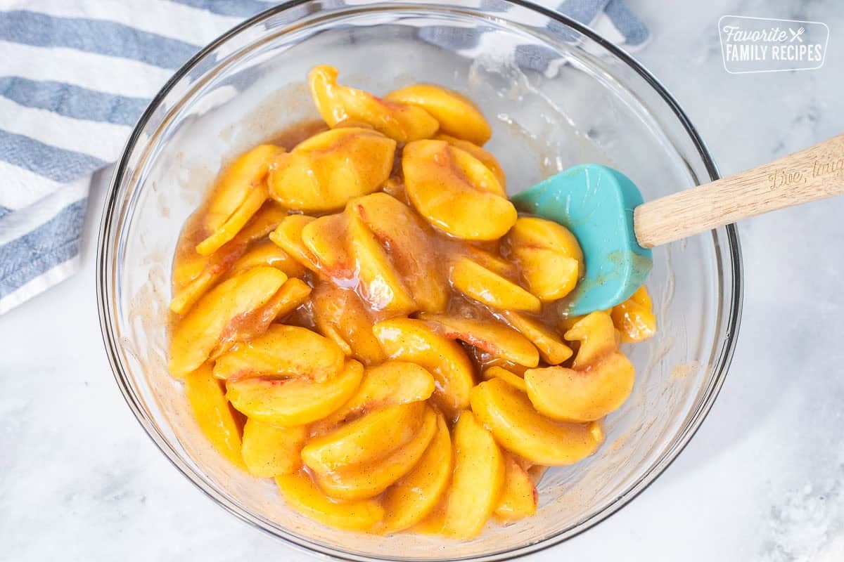 Mixing fresh peaches with hot cinnamon glaze in a bowl to make a homemade peach pie filling.