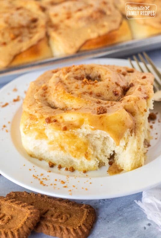 Biscoff Cinnamon Roll on a plate frosted with Biscoff frosting and cookie crumbles on top.