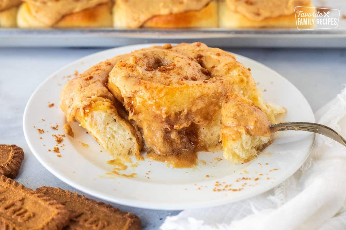 Center of Biscoff Cinnamon Roll on a plate frosted with Biscoff frosting and cookie crumbles on top.