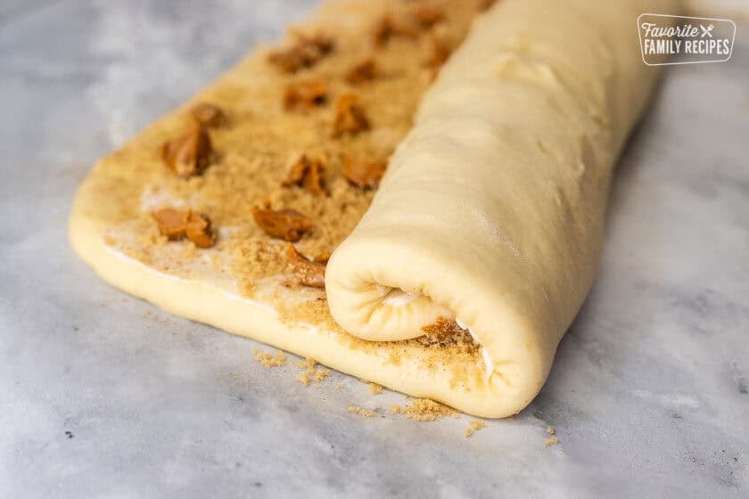 Rolled up cinnamon roll dough with butter, sugars, cinnamon and Biscoff cookie butter drops in the middle.