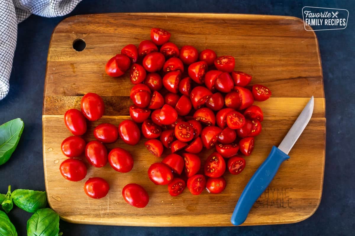Cutting board with sliced cherry tomatoes and a knife.