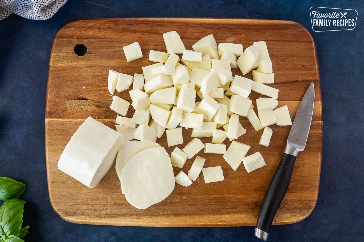 Cutting board with cubed fresh mozzarella cheese and a knife.