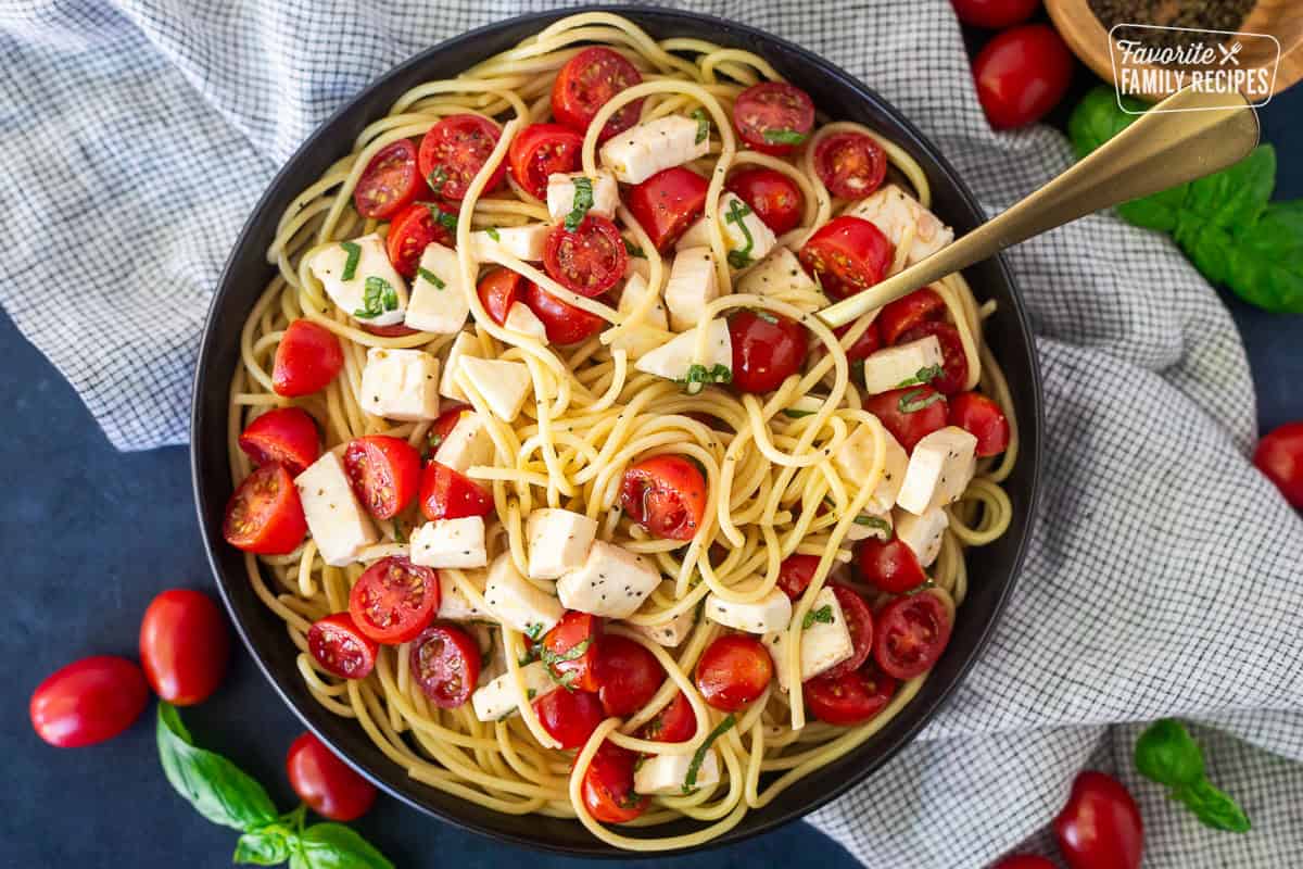 Spaghetti noodles with a half cherry tomato, mozzarella and basil.