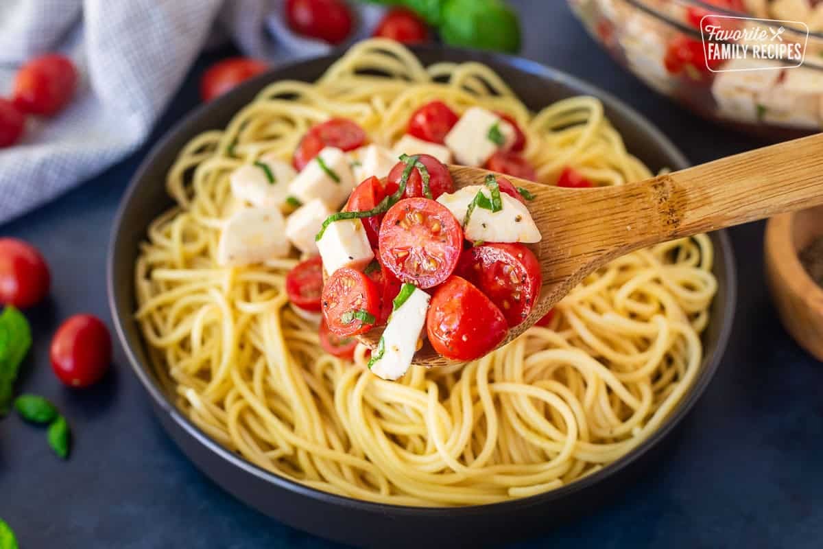 Wooden spoon with Tomato Basil Pasta with spaghetti noodles, cherry tomatoes, mozzarella cheese and fresh basil in an olive oil vinegar dressing.