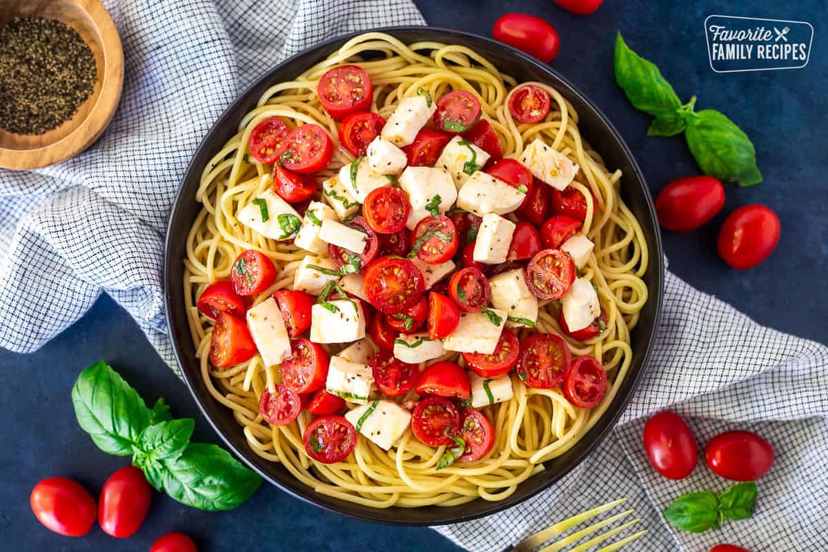 Wooden spoon with Tomato Basil Pasta with spaghetti noodles, cherry tomatoes, mozzarella cheese and fresh basil in an olive oil vinegar dressing.