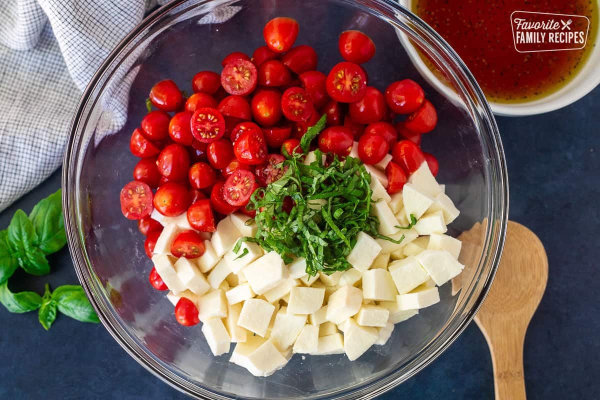 Glass bowl with cherry tomatoes cut in half, cubed fresh mozzarella cheese and finely sliced fresh basil. Dressing mixed in a bowl on the side.