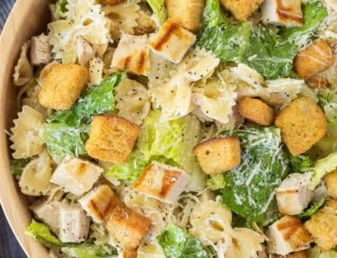 Bowl of chicken caesar pasta salad with romaine lettuce, croutons, bow tie pasta, grilled chicken and fresh parmesan cheese.