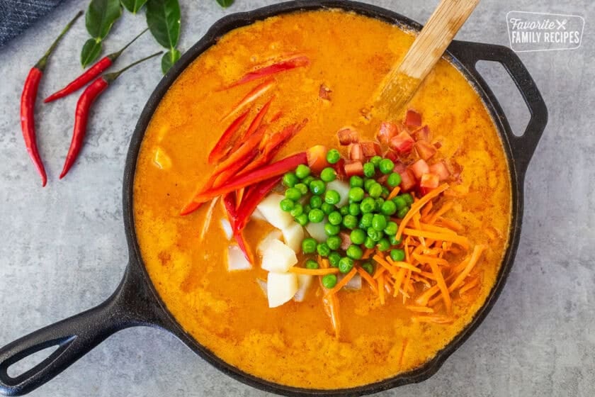 Cooking Panang curry in a skillet with a wooden spoon.