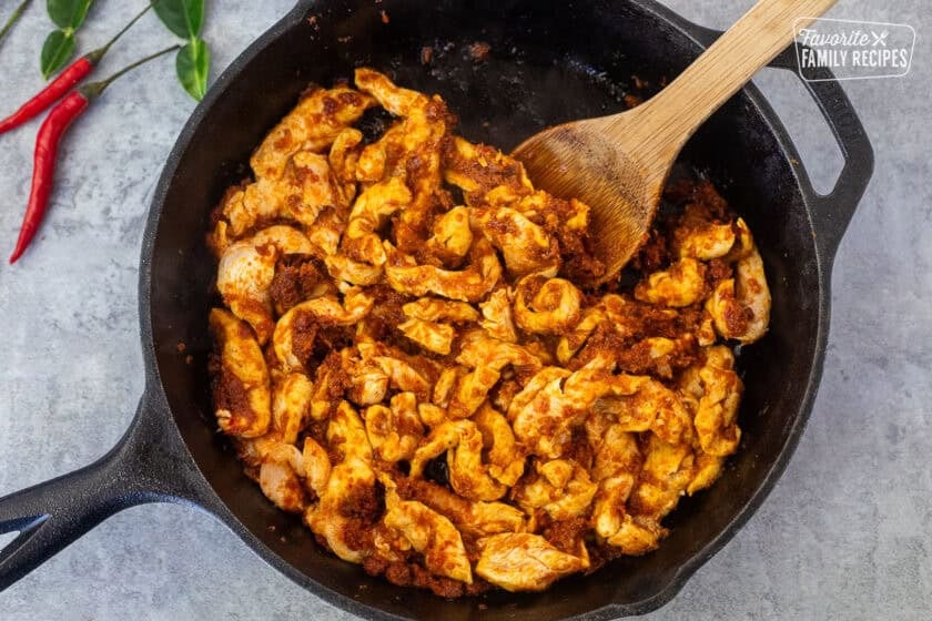 Panang curry and chicken cooking in a skillet with a wooden spoon.