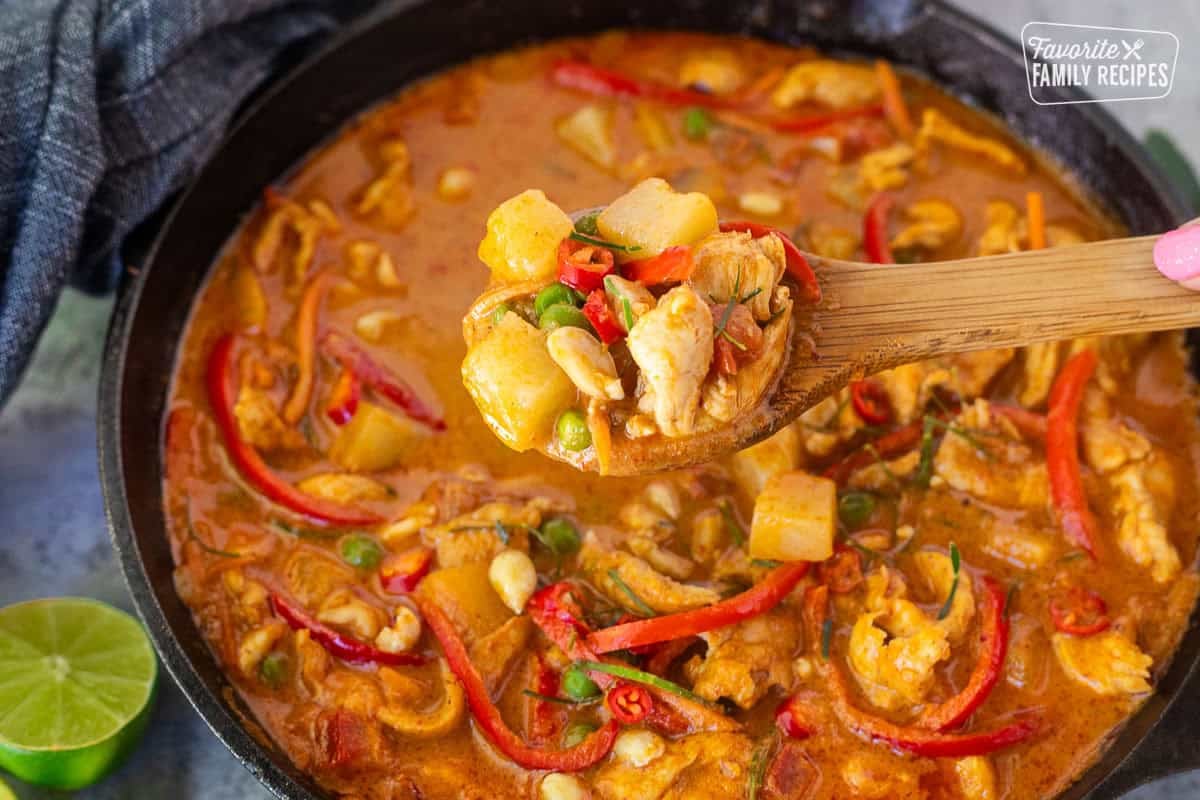 Wooden spoon with chicken Panang curry including red bell peppers, peas, potatoes, tomatoes, peas and carrots.