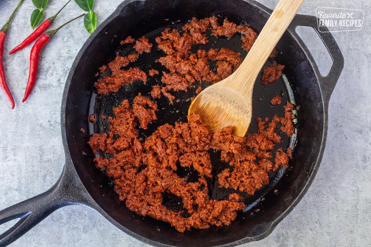 Skillet with oil and parang curry paste with wooden spoon.