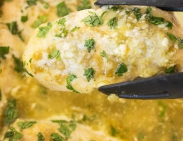 Tongs holding up a salsa verde chicken breast topped with cilantro.