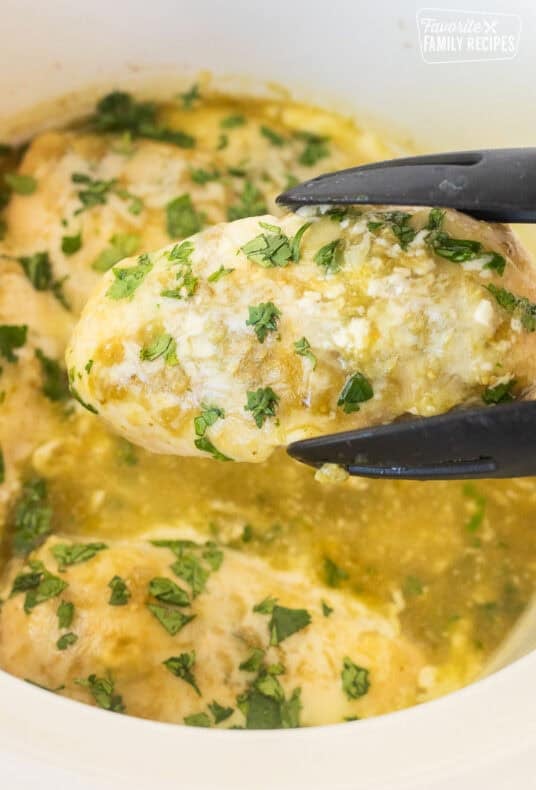 Tongs holding up a salsa verde chicken breast topped with cilantro.