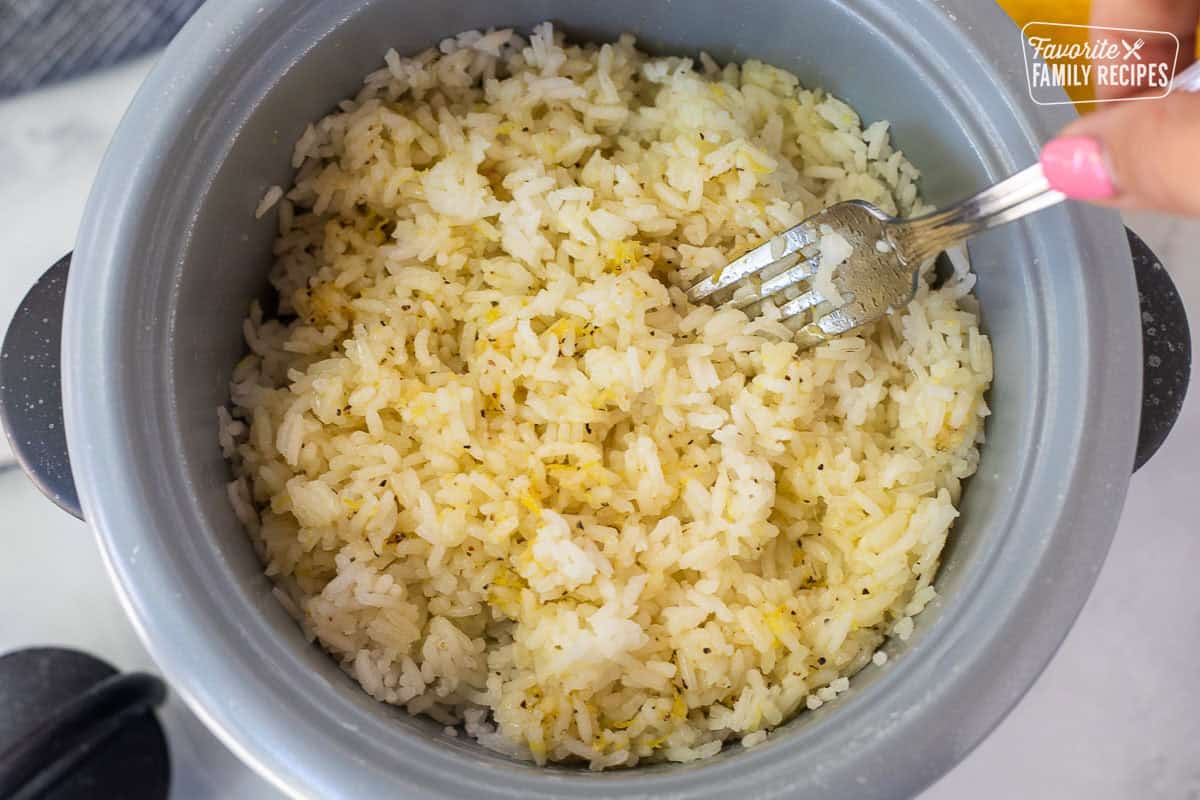 Mixing lemon rice with a fork in rice cooker.