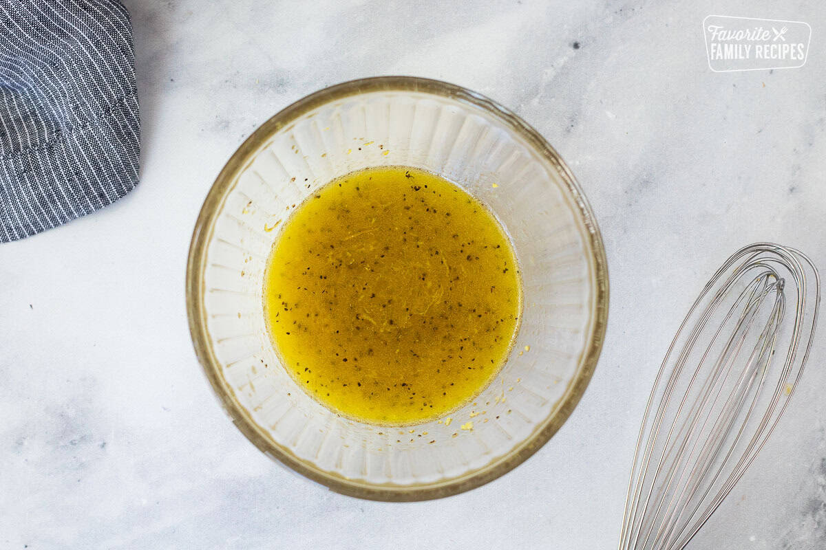 Glass bowl with lemon juice mixture and whisk on the side.