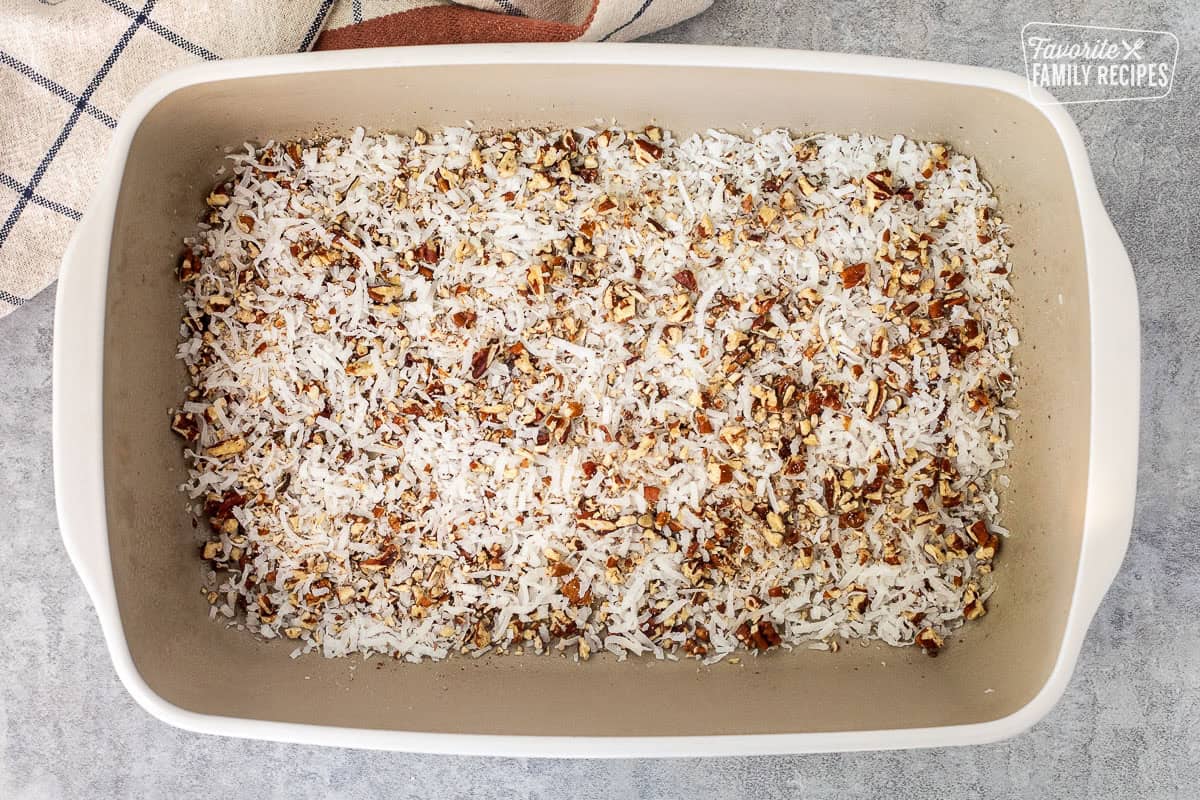 Baking dish with chopped pecans and coconut flakes in the bottom.