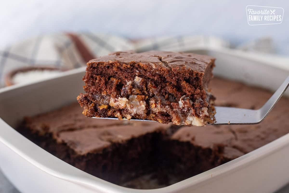 This German Chocolate Upside Down Cake Recipe is a fun twist on a classic. It has a crunchy bottom layer, a creamy middle layer, and a fudgy top layer. Slice of German Chocolate upside down cake on a spatula.