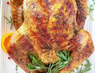 Thanksgiving turkey on a platter with sage, thyme and orange slices.