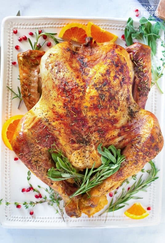 Thanksgiving turkey on a platter with sage, thyme and orange slices.