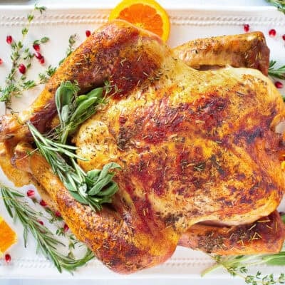 Thanksgiving turkey on a platter with sage, thyme and orange slices.
