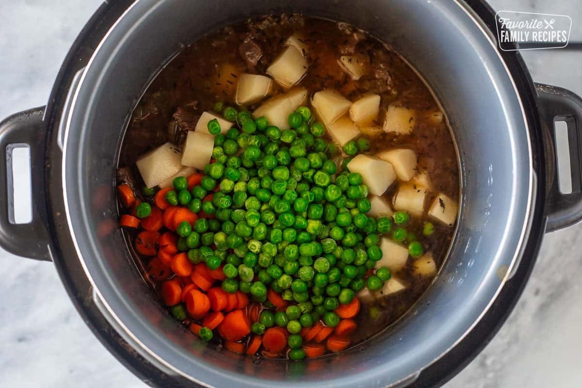 Instant pot with cooked beef, cut potatoes, peas and carrots.